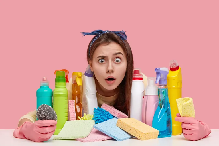 young-woman-with-unexpected-gaze-wears-headband-has-many-detergents-table-shocked-wth-dirty-room-wears-protective-gloves