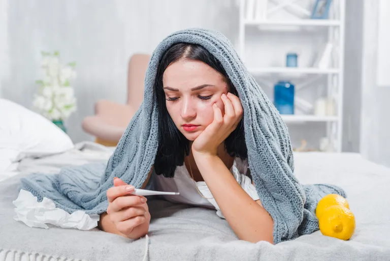 young-woman-with-scarf-around-her-head-checking-fever-with-thermometer