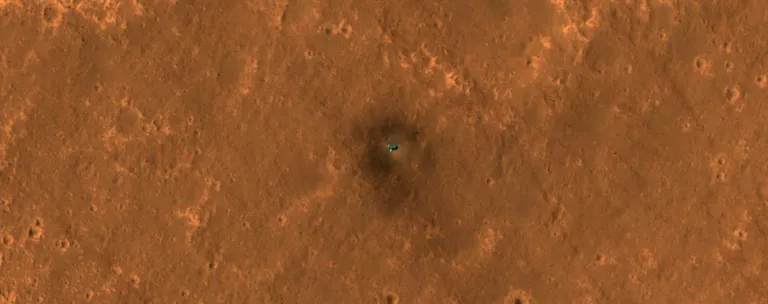 ภาพถ่ายของยาน InSight จากกล้อง HiRISE ของยาน MRO ที่ถ่ายไว้เมื่อปี 2019 จะเห็นได้ว่ายาน InSight ในเวลานั้นยังมีสีสันที่ตัดกับพื้นผิวดาวอังคารชัดเจนเพราะฝุ่นยังไม่มาเกาะบดบังแสงอาทิตย์มากนัก ภาพจาก NASA_JPL.jp