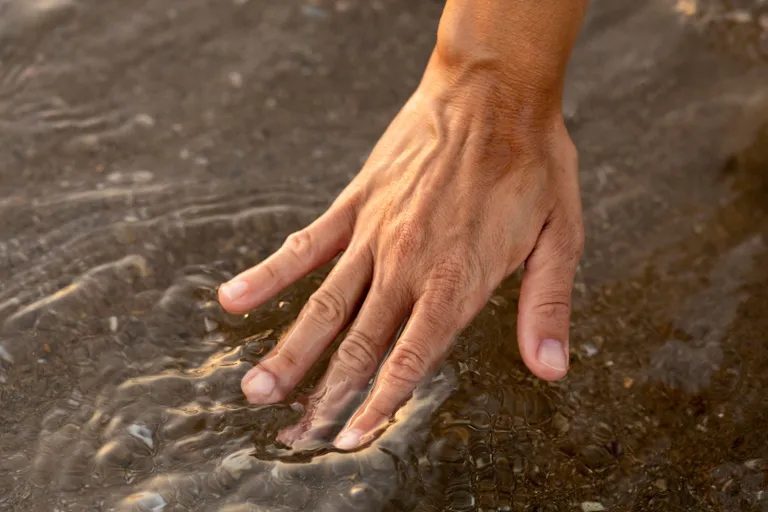person-putting-their-hand-water-beach