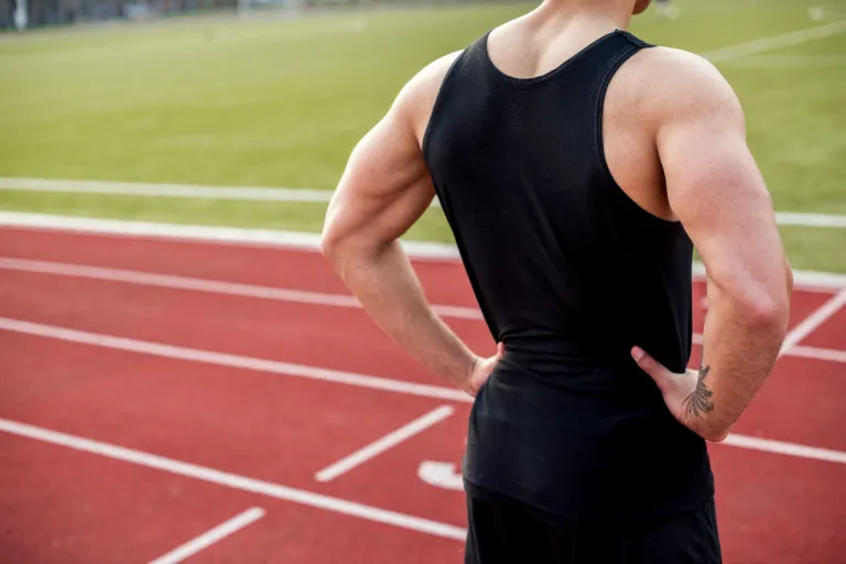 rear-view-male-athlete-with-hands-hip-standing-race-track