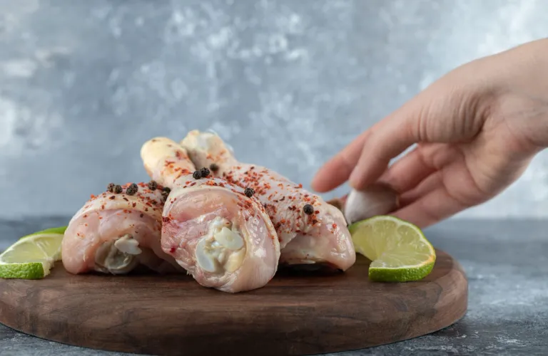 female-hand-putting-lime-slices-side-marinated-chicken-legs-grey