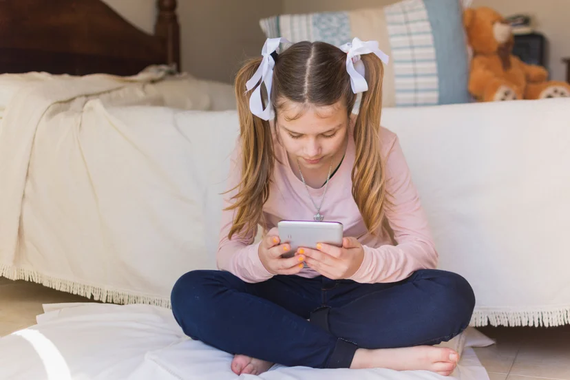 girl-sitting-pillow-looking-mobile-phone-bedroom