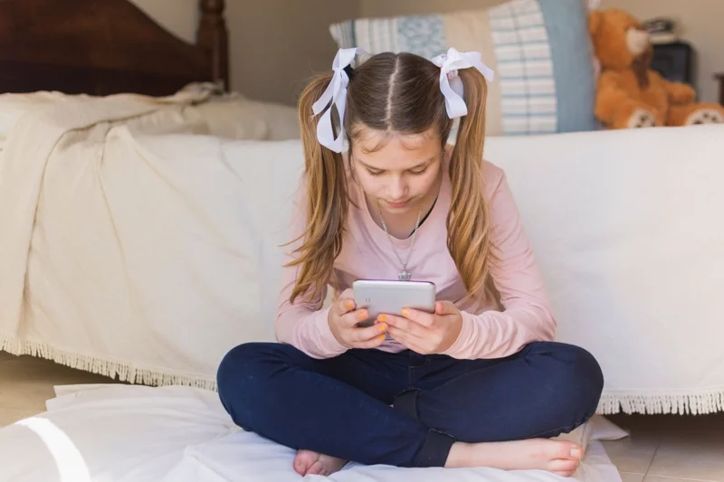 girl-sitting-pillow-looking-mobile-phone-bedroom